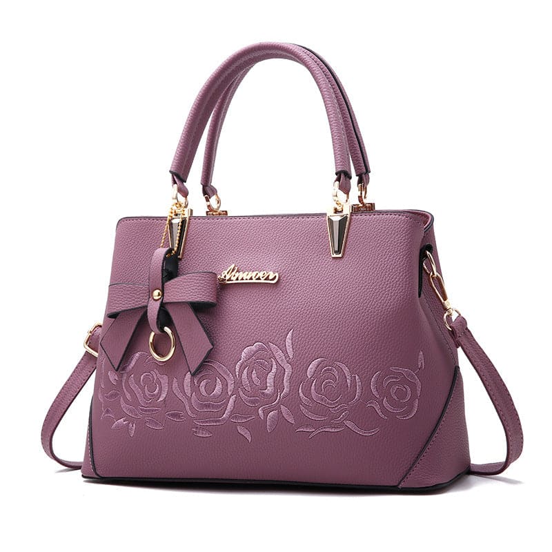 Purple leather handbag with embossed rose design and bow accent.