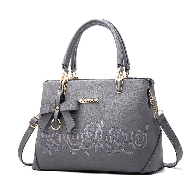 Gray leather handbag with embossed floral design and gold hardware.