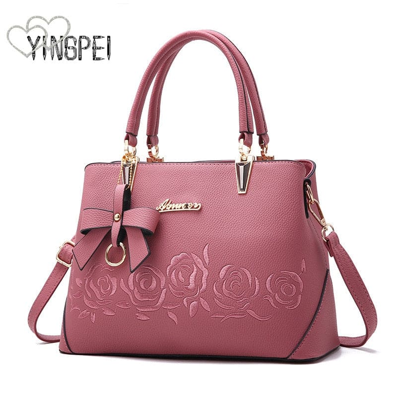 Pink leather handbag with embossed rose design and bow accent.