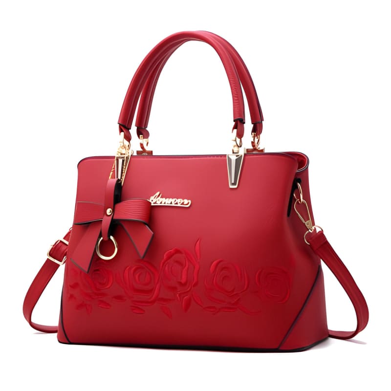 Red leather handbag with embossed floral design and bow accent.