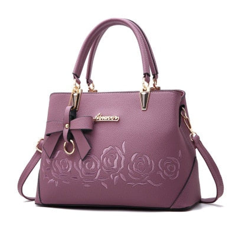Purple leather handbag with embossed rose design and bow accent.