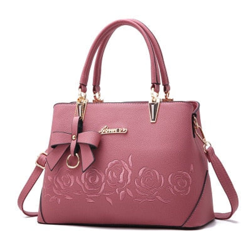 Pink leather handbag with embossed rose design and bow accent.