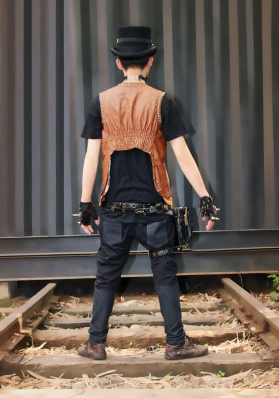 Person wearing a black hat, dark shirt, orange vest, and jeans standing on railroad tracks.