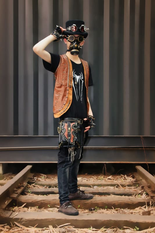 Person wearing steampunk-inspired goggles and eclectic clothing standing on railroad tracks.