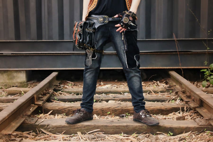 Person wearing jeans and a tool belt standing on railroad tracks.