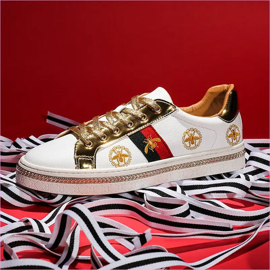 Designer sneaker with white, gold, and red accents featuring bee emblems.