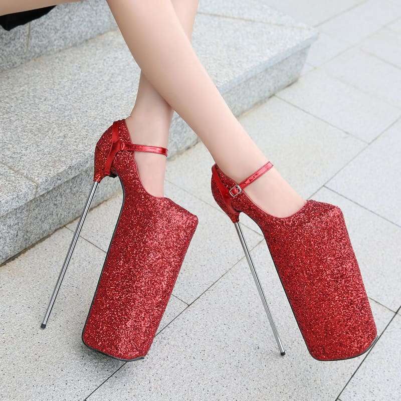 Pair of extremely high platform stiletto shoes in glittery red with ankle straps and metallic spike heels.
